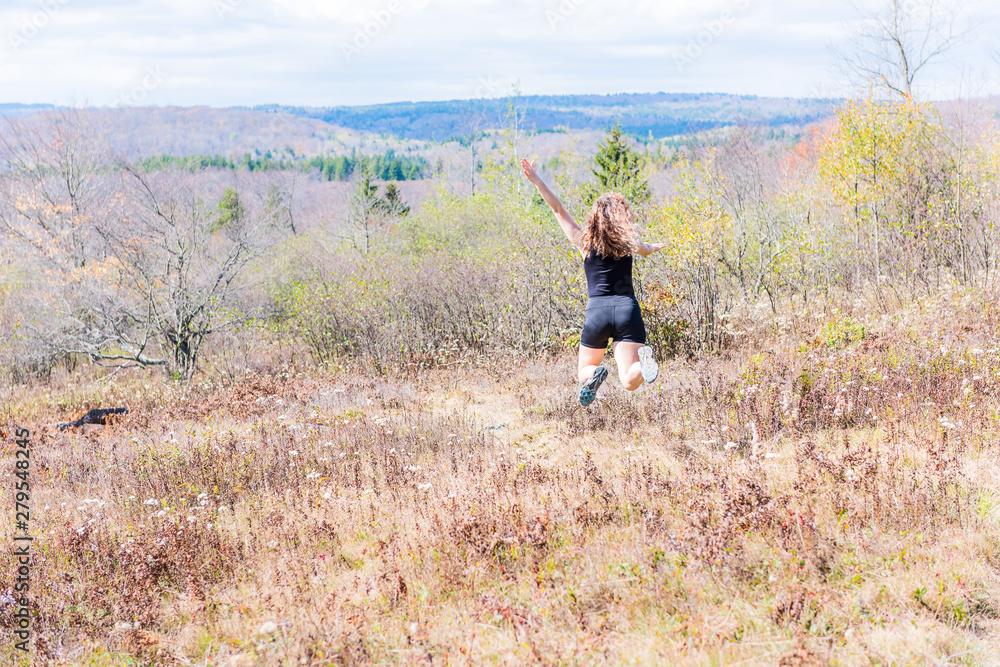 Young athletic, fit, free happy woman running jogging jumping in autumn, fall, summer meadow field path hike in mid-air, muscles