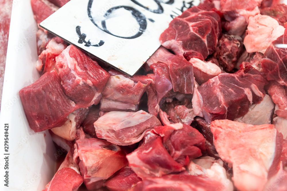 Closeup of many beef meat chunks, cut in slices on retail display store, shop in butchers shopping area in fridge, refrigerated with price tag, label