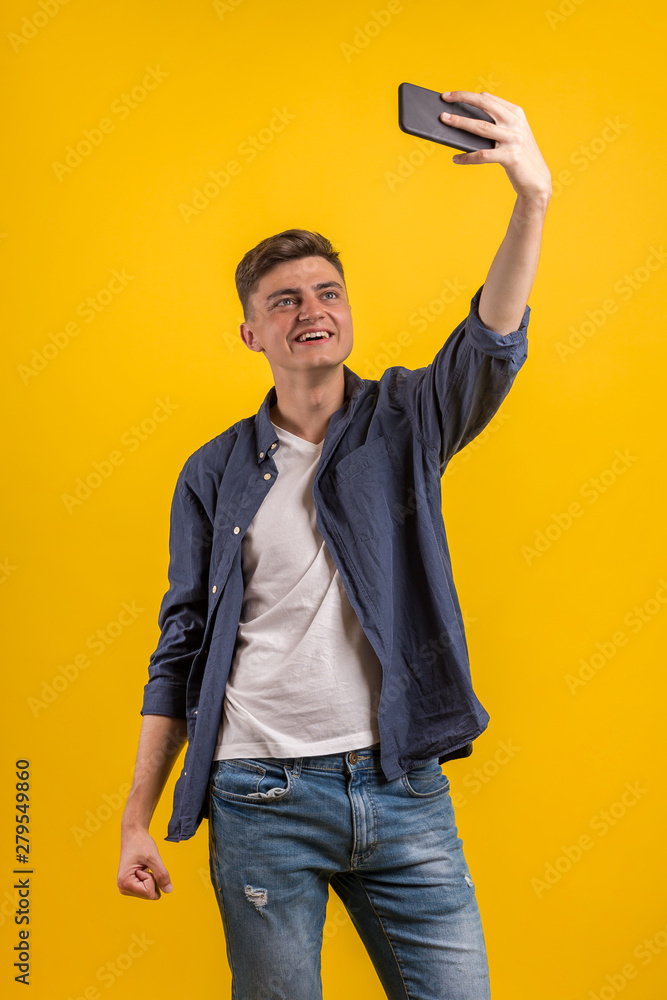 Cheerful young man wearing plaid shirt standing isolated over orange background, taking a selfie 
