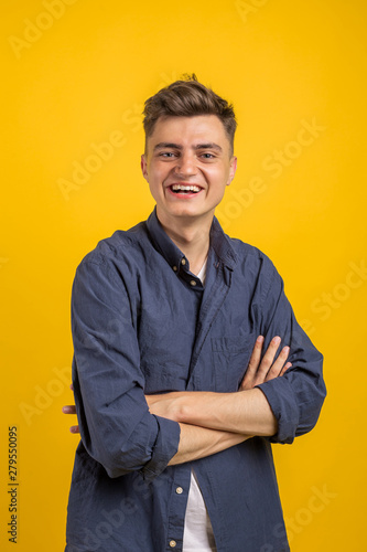 Portrait of happy young man with crossed arms standing over yellow background and looking at camera