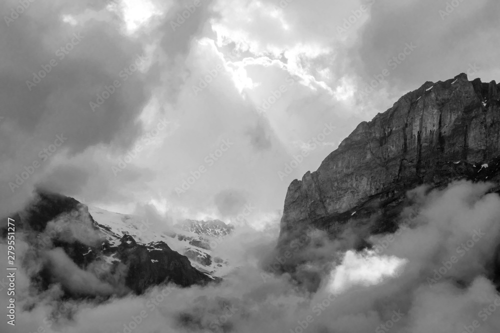 Black and white photo of hight Alps mountains and white clody sky with sunlight