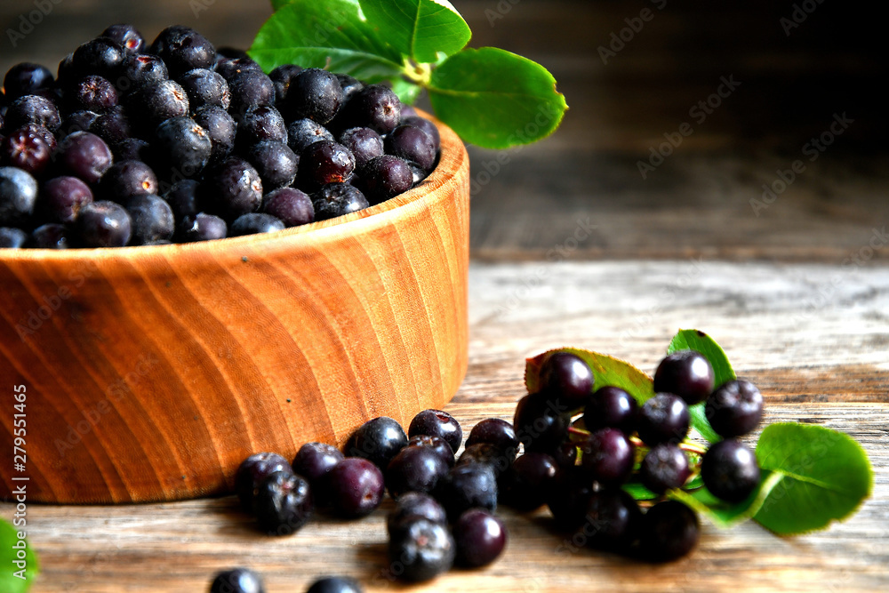 Black chokeberry in wooden utensils on old wooden boards. Black chokeberry in wooden utensils on old wooden boards.