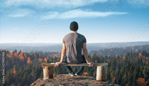 Mężczyzna siedzi na punkcie widokowym nad lasem. Widok z tyłu.