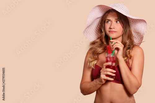 Picture of upset attractive female having unpleasant facial expression, looking aside, being on holidays, holding cocktail, spending time alone, having long fair hair. Copy space for advertisement.