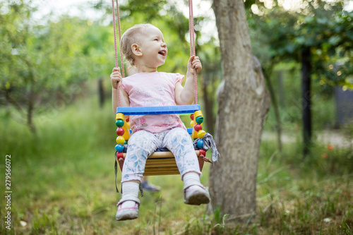 Happy little girl on swing in summer garden