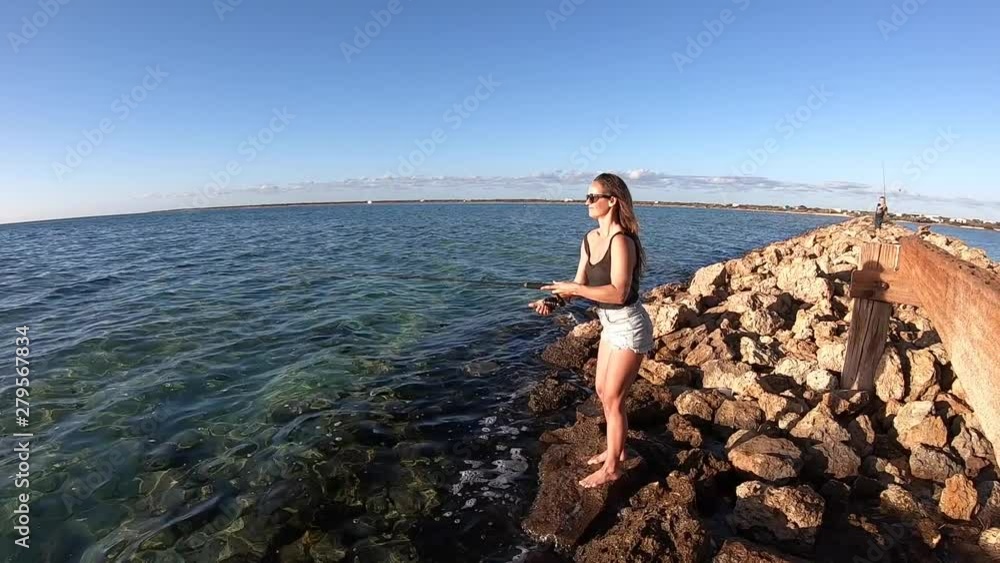 Young woman casting and fishing from rocks in Australia Young woman casting and fishing from rocks in Australia