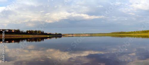 Bright reflection of the sky and banks in the Northern river vilyu in Yakutia at sunset in the evening in the spruce forest and the village houses.