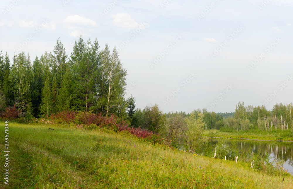 The road overgrown with grass goes along the field and the water of the lake in autumn in the colorful sparse Northern vegetation. The road overgrown with grass goes along the field and the water of the lake in autumn in the colorful sparse Northern vegetation.