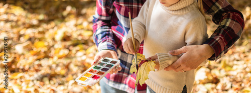 Girl and her mother enjoy autumn season. Drawing with paint autumn leaves outside