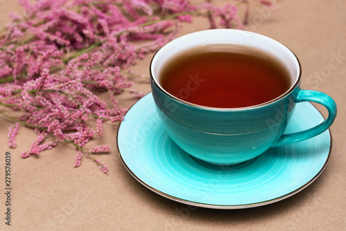 Cup of hot tea and a tamarix gallica tree branches on a brown background.