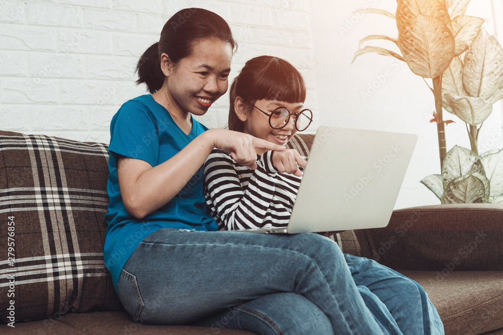 Young Asian girl kid with mom use laptop on sofa. Learning and searching internet, family activity at home Young Asian girl kid with mom use laptop on sofa. Learning and searching internet, family activity at home
