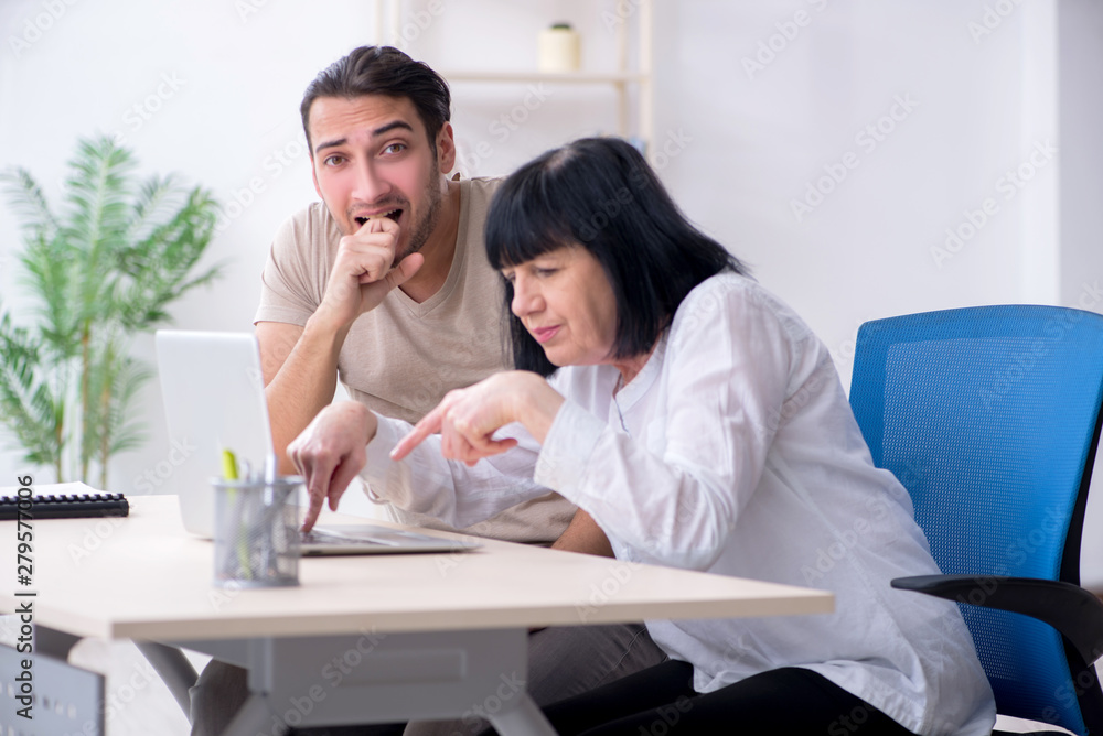 Young male employee explaining to old female colleague how to us Young male employee explaining to old female colleague how to us