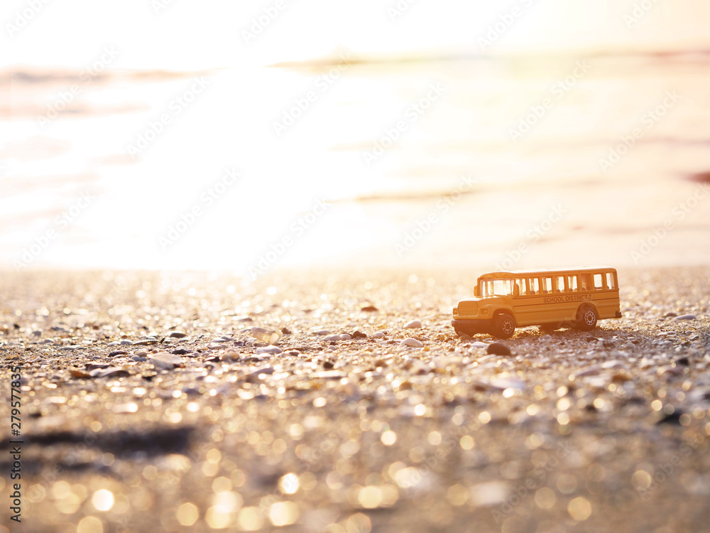 Naklejka premium Close up yellow school bus toy on sand at sunset beach.