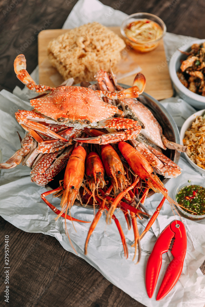 Top view of steamed Flower Crabs and Grilled Prawns (Shrimps) with Crab Cracker on paper with other seafoods in background. Top view of steamed Flower Crabs and Grilled Prawns (Shrimps) with Crab Cracker on paper with other seafoods in background.