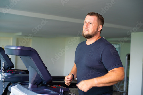 sad full male runs on a treadmill in a gym. concept of weight loss and sport. side view.