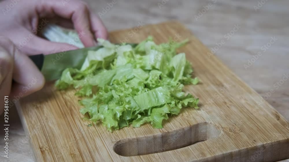 Slices of greengrocery. Female hands cut lettuce leaves on a wooden cutting board. Slices of greengrocery. Female hands cut lettuce leaves on a wooden cutting board.