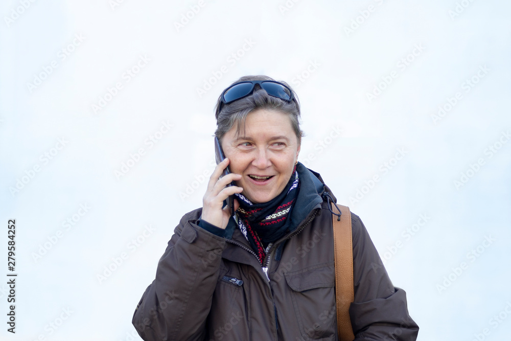 A middle-aged woman cheerfully talks on the phone at bright background A middle-aged woman cheerfully talks on the phone at bright background
