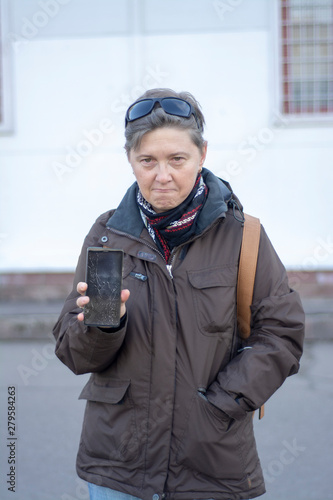 Upset middle-aged woman demonstrates the broken screen of a modern mobile phone photo