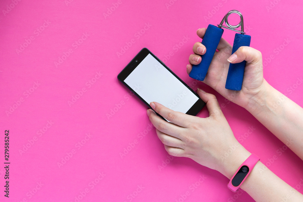 Fitness tracker on a womans hand, smartphone and sports accessories on pink background. Fitness tracker on a womans hand, smartphone and sports accessories on pink background.