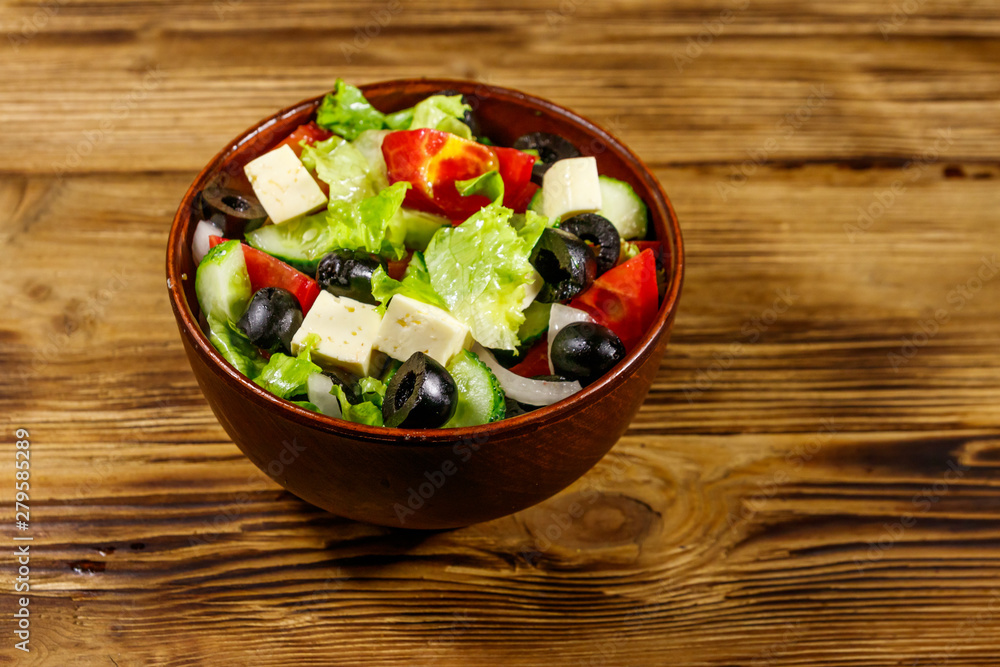 Greek salad with fresh vegetables, feta cheese and black olives on wooden table