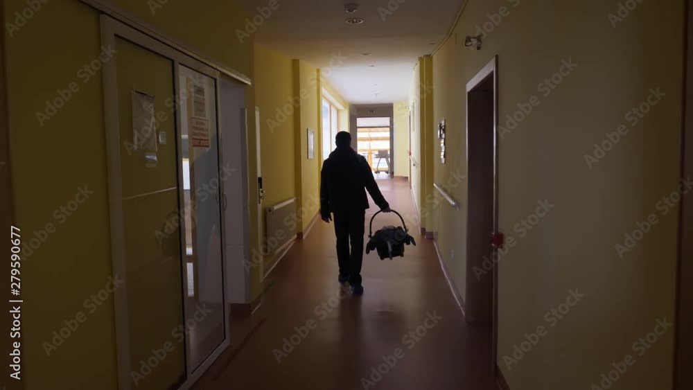 Father silhouette with back carrying newborn in car seat going outside hospital Father silhouette with back carrying newborn in car seat going outside hospital