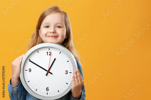 A cute little girl holding a big clock over a yellow background. The concept of education, school, timing, time to learn. Copy space.