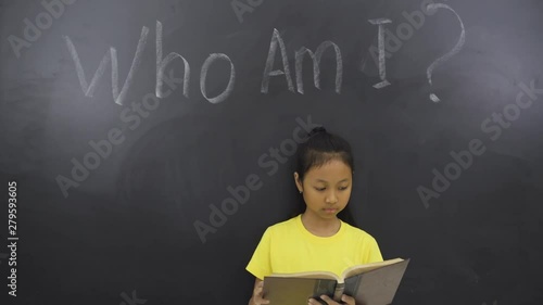 Female elementary student reading a book in the class with text of Who Am I? photo