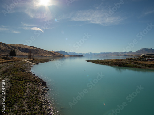 View of Lake Tekapo, New Zealand, with turquoise blue water and sun flare
