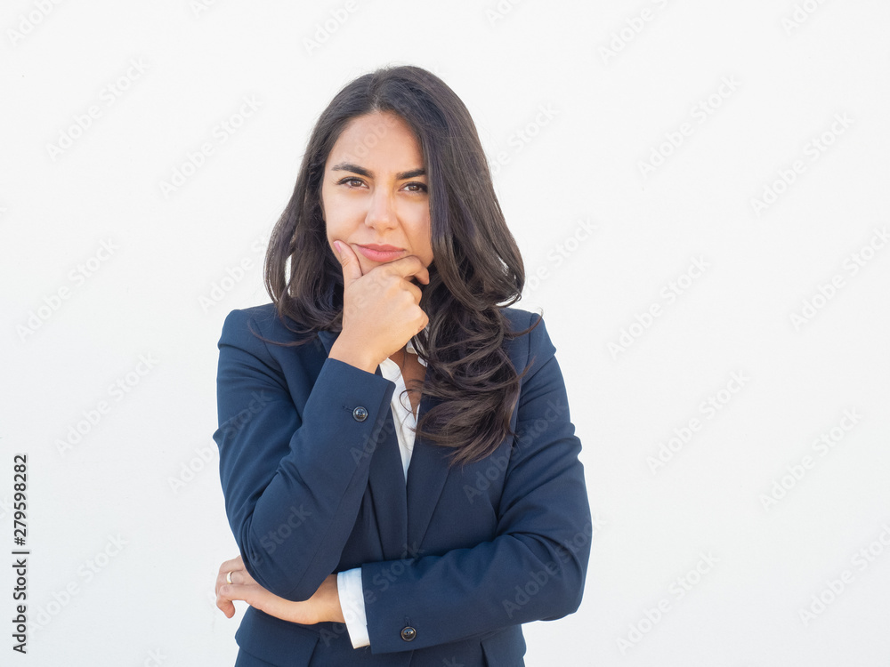 Pensive office employee thinking hard. Thoughtful calm young Latin business woman in office jacket leaning chin on hand and looking at camera. Wondering concept Pensive office employee thinking hard. Thoughtful calm young Latin business woman in office jacket leaning chin on hand and looking at camera. Wondering concept