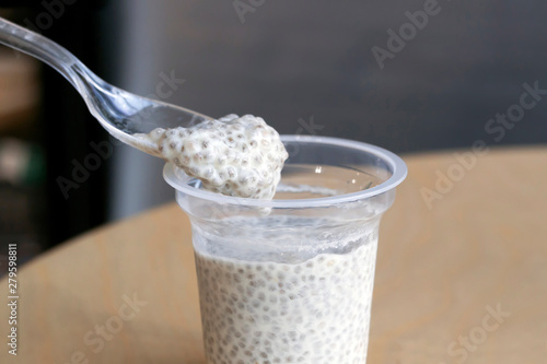Taking spoon of chia seeds with coconut milk pudding from plastic cup on wooden table in cafe. Healthy food concept. Close-up, copy space