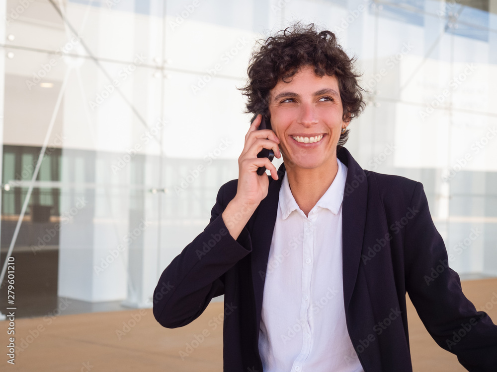 Happy successful androgynous businesswoman enjoying phone call outdoors. Joyful young woman in jacket talking on cellphone near office building. Good news concept Happy successful androgynous businesswoman enjoying phone call outdoors. Joyful young woman in jacket talking on cellphone near office building. Good news concept