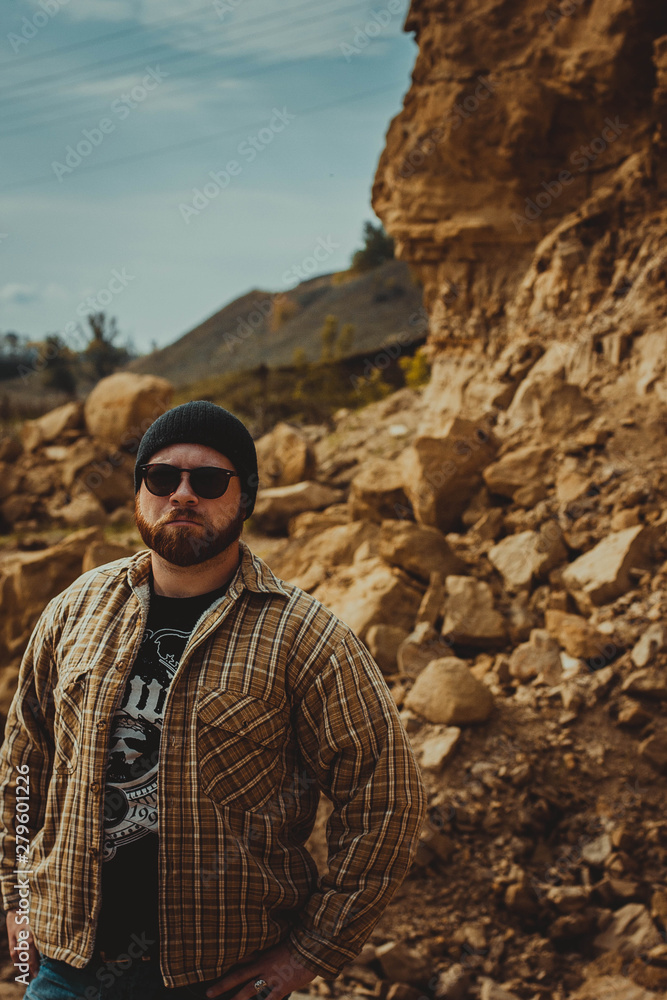 brutal man in glasses and a hat on the background of rocks brutal man in glasses and a hat on the background of rocks