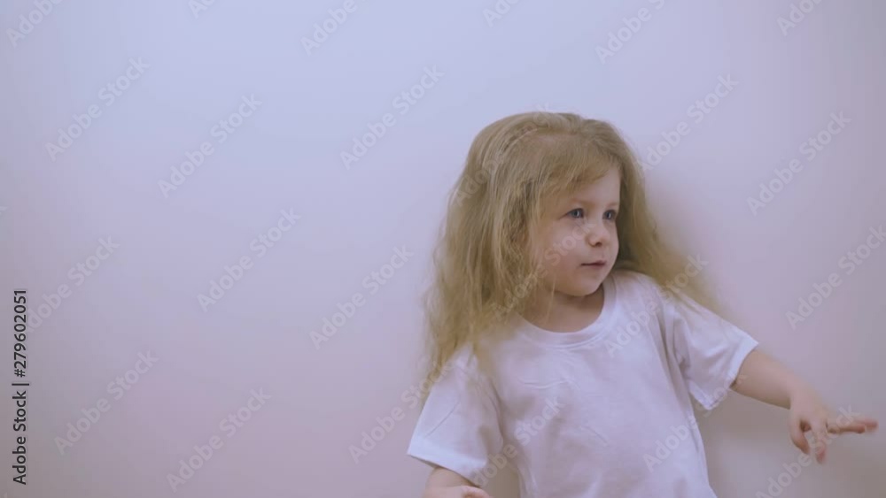 adorable little girl with blond loose hair in t-shirt dances posing at bright light in white background closeup adorable little girl with blond loose hair in t-shirt dances posing at bright light in white background closeup