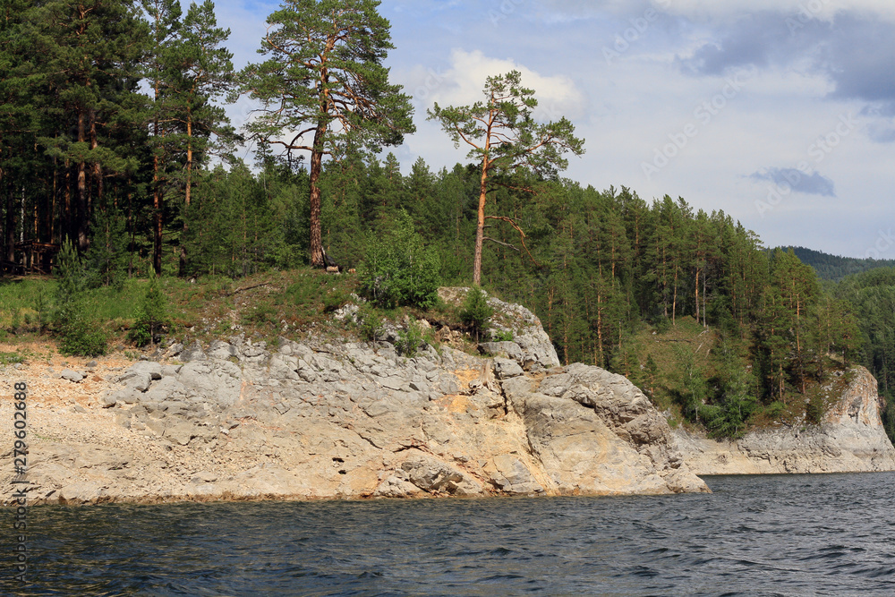 View of the Yenisei River and the rocky shore with trees lit by the sun.