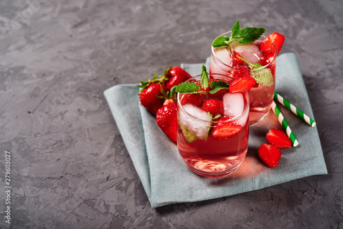 Fresh strawberry lemonade with ice, mint and paper straw in sparkling glasses on gray table background, copy space. Cold summer drink. Berry cocktail photo