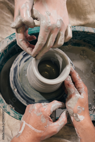 Man and woman hands pottery studying in studio. Creating vase. Hands in the clay and the potter's wheel with the product. Pottery class from above.