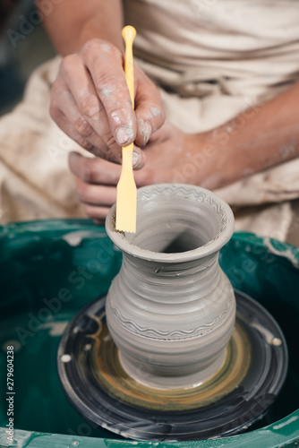 Close up on hands , potter working on the wheel shaping clay making vase. Hand with pottery making tools, cutting and shaping. photo