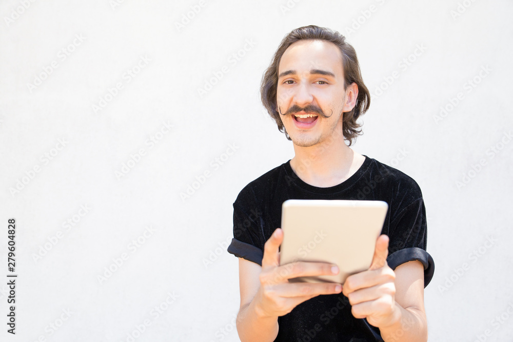 Happy man wearing velvet t-shirt holding tablet. Smiling stylish hipster guy with tablet posing. Technology concept Happy man wearing velvet t-shirt holding tablet. Smiling stylish hipster guy with tablet posing. Technology concept