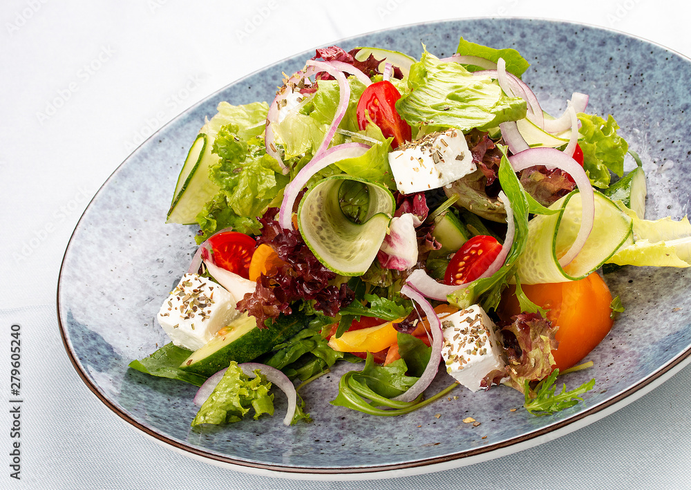 Classic Greek salad of tomatoes, cucumbers, red pepper, onions with olives, oregano and feta cheese. On a decorative plate
