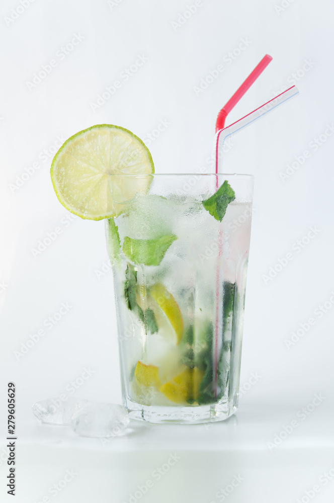 Mojito cocktail in a transparent glass with ice. Recipe for exotic drinks with mint, lime and white rum. Glass with a cocktail on a white background in the rays of the sun. Mojito cocktail in a transparent glass with ice. Recipe for exotic drinks with mint, lime and white rum. Glass with a cocktail on a white background in the rays of the sun.