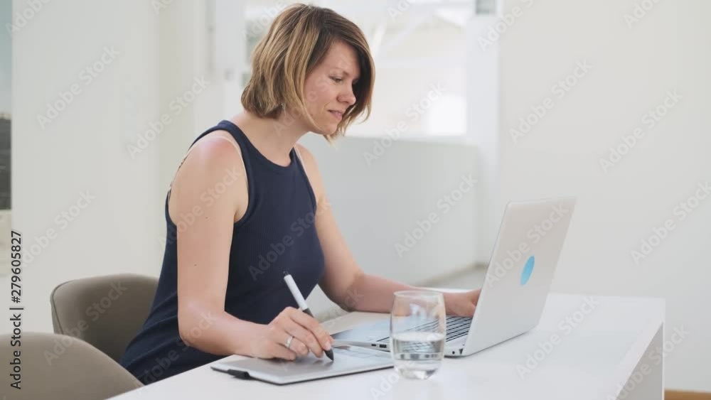 Young white female designer working on a laptop using a graphic pen tablet Young white female designer working on a laptop using a graphic pen tablet