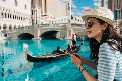 Tourist woman travel in Italy. View on Grand canal with gondola boat sailing and moving on it. Young girl with straw hat and sunglasses smiling using mobile phone while relax enjoy view in venice. © PR Image Factory