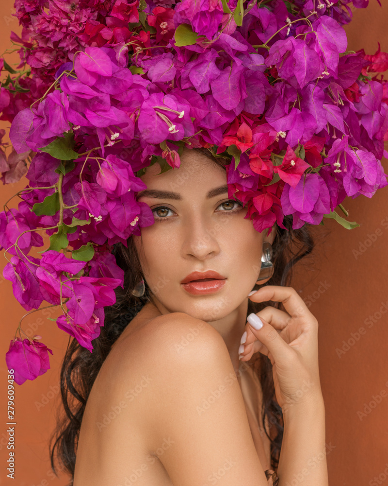 Beauty fashion model girl with pink flower on her head. Portrait on red orange background. Spa and beauty salon concept.