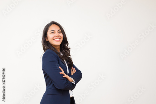 Young businesswoman smiling at camera. Portrait of beautiful happy young woman standing with crossed arms and looking at camera isolated on grey background. Emotion concept photo