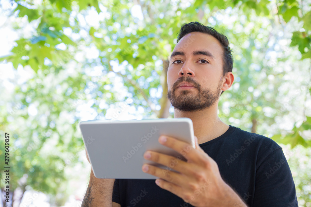 Bearded man using tablet pc outdoor. Low angle view of handsome young man holding digital tablet. Wireless technology concept Bearded man using tablet pc outdoor. Low angle view of handsome young man holding digital tablet. Wireless technology concept