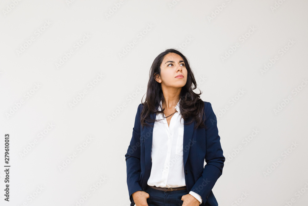 Confident businesswoman with hands in pockets looking up. Professional confident young businesswoman standing with hands in pockets isolated on grey background. Business concept Confident businesswoman with hands in pockets looking up. Professional confident young businesswoman standing with hands in pockets isolated on grey background. Business concept