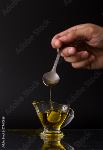  hold with olive spoon with glass bowl with extra virgin olive oil on black background