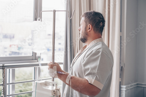 A man stands in a hospital ward and looks out the window. Dropper in a mans hand in a hospital.