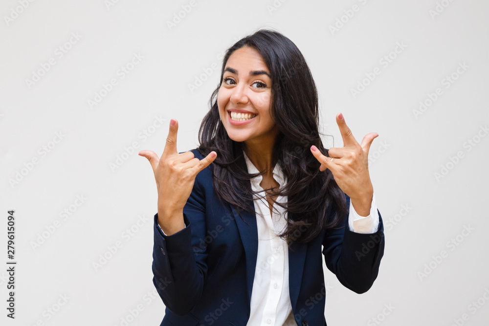 Happy businesswoman gesturing with hands. Excited young woman showing rock n roll symbol and smiling at camera isolated on grey background. Emotion concept Happy businesswoman gesturing with hands. Excited young woman showing rock n roll symbol and smiling at camera isolated on grey background. Emotion concept