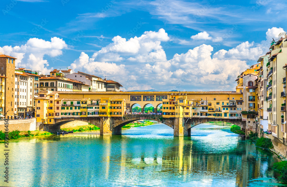 Ponte Vecchio stone bridge with colourful buildings houses over Arno River blue turquoise water and embankment promenade in historical centre of Florence city, blue sky white clouds, Tuscany, Italy